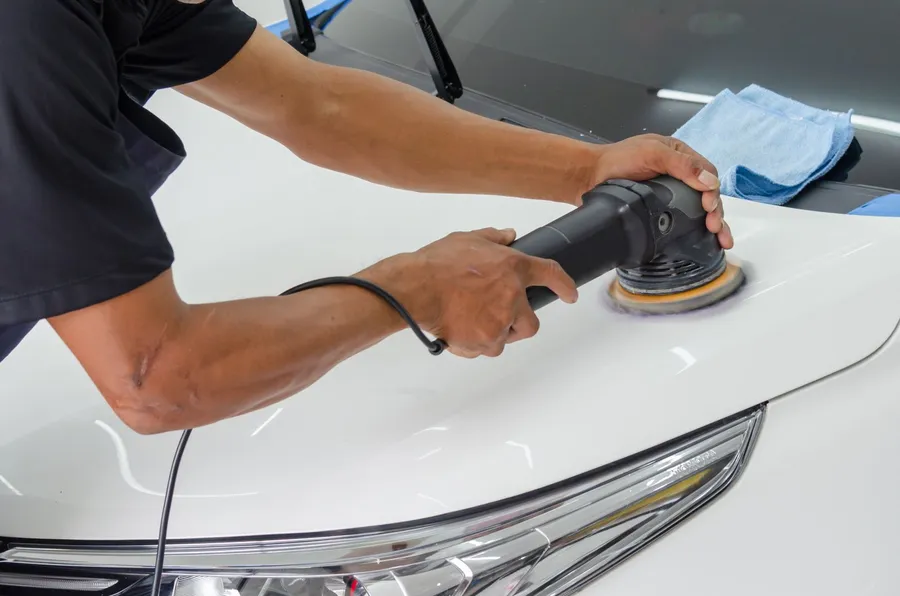 Technician machine polishing a white car hood during paint correction